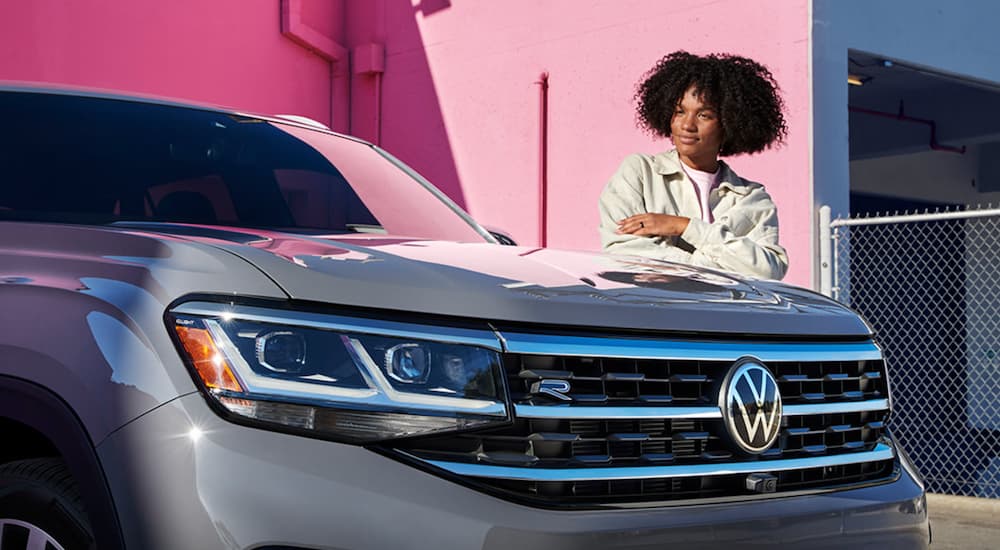A person is shown standing behind a 2022 Volkswagen Atlas Cross Sport V6 SEL Premium R-Line parked in front of a pink wall.