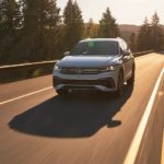 A silver 2022 Volkswagen Tiguan is shown driving on a road past a lake.