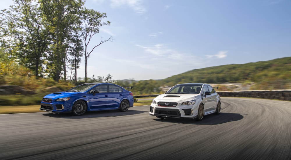 A blue and a white 2019 Subaru WRX STI S209 are driving side by side on an empty road.