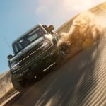A green 2021 Ford Bronco Wildtrak is shown kicking up sand on a dune.