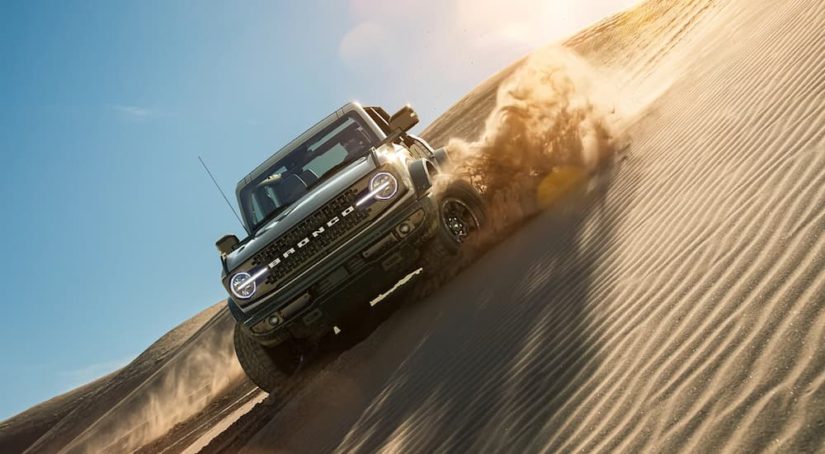 A green 2021 Ford Bronco Wildtrak is shown kicking up sand on a dune.