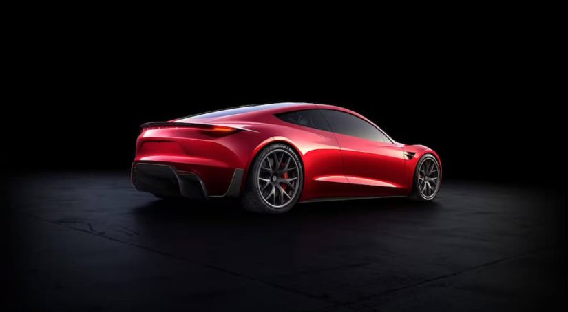 A red 2023 Tesla Roadster is shown from the rear parked against a black background.
