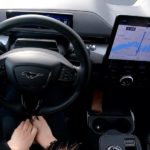 The black interior of a 2022 Ford Mustang Mach-E shows the steering wheel and infotainment screen.