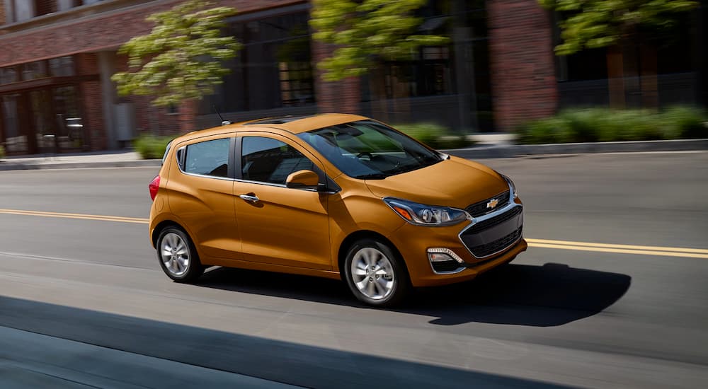 An orange 2020 Chevy Spark is shown leaving a certified pre-owned Chevy dealer.