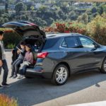 A family is shown sitting in the rear cargo space of a grey 2021 Chevy Equinox.