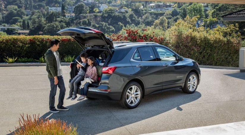 A family is shown sitting in the rear cargo space of a grey 2021 Chevy Equinox.
