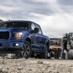 A blue 2020 Ford F-150 is shown from the front while parked next to two UTVs on a trail.