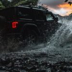 A black Certified Pre-Owned Jeep, a 2020 Jeep Wrangler unlimited is shown off-roading through a river.