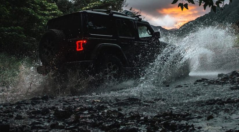 A black Certified Pre-Owned Jeep, a 2020 Jeep Wrangler unlimited is shown off-roading through a river.