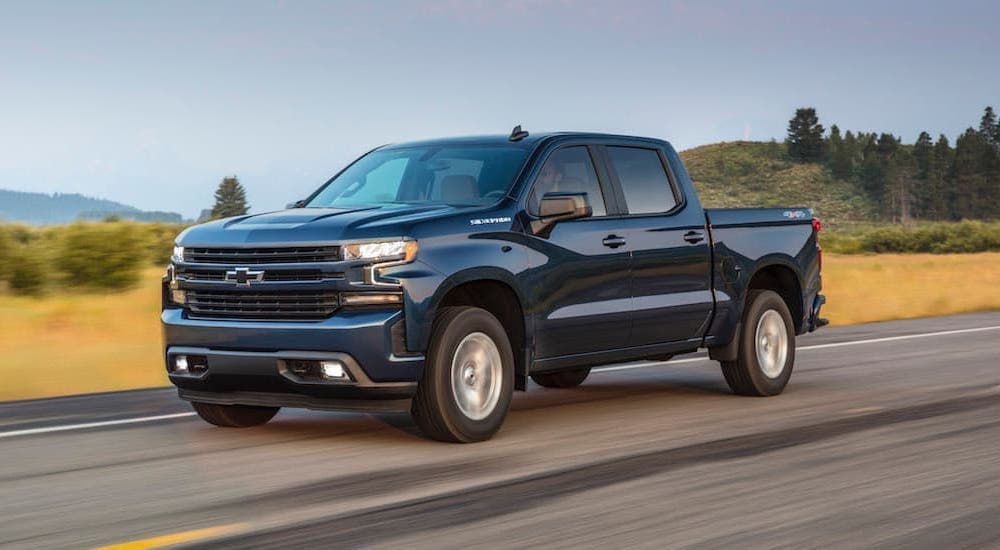A popular Certified pre-owned Chevy, a blue 2020 Chevy Silverado 1500 is shown from the side driving on an open road.