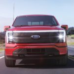 A red 2022 Ford F-150 Lightning is shown from the front driving on an empty road.
