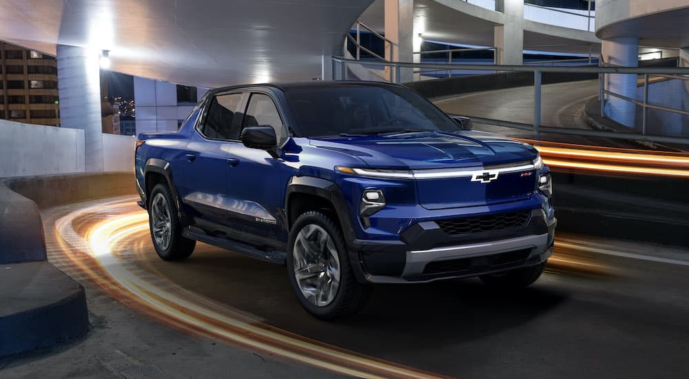 A blue 2024 Chevy Silverado EV RST is shown driving on a ramp in a parking garage.