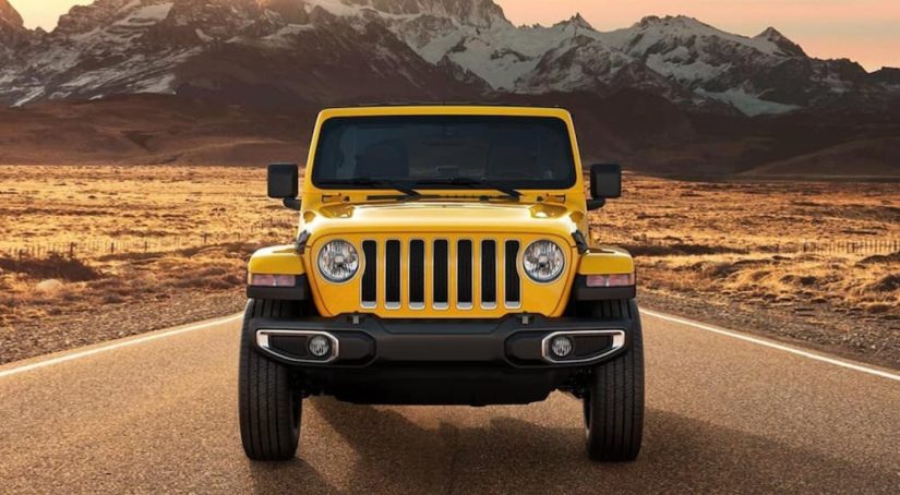 A yellow 2021 Jeep Wrangler is shown from the front parked on a desert highway.