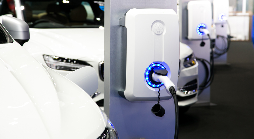 A row of white vehicles are shown parked at charging stations.