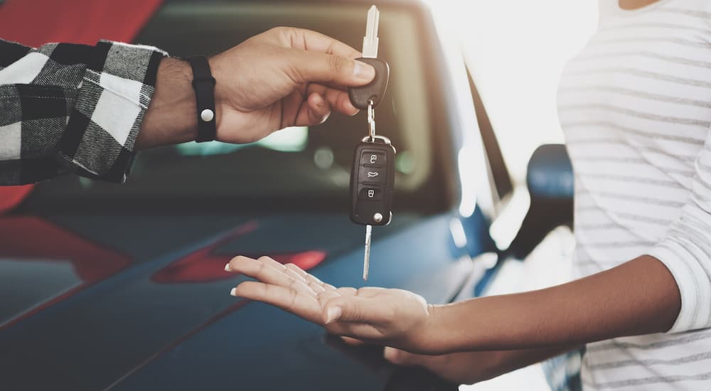 A person is passing a set of car keys to another person after finding the best used car.