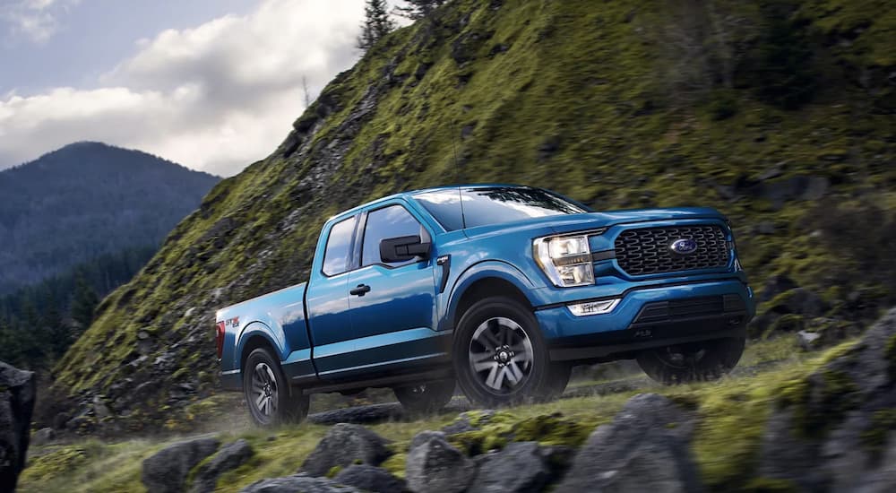 A blue 2021 Ford F-150 STX is shown driving up a mountainside trail.