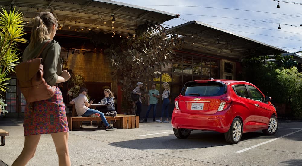 A woman is shown walking towards a red 2022 Chevy Spark LT near a coffee shop.