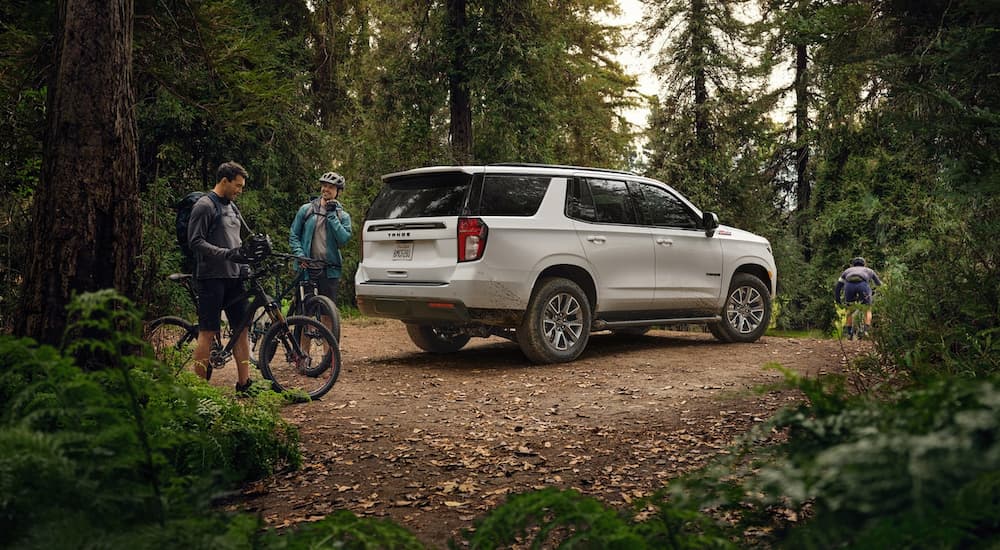 A white 2022 Chevy Tahoe is shown in the woods near people biking.