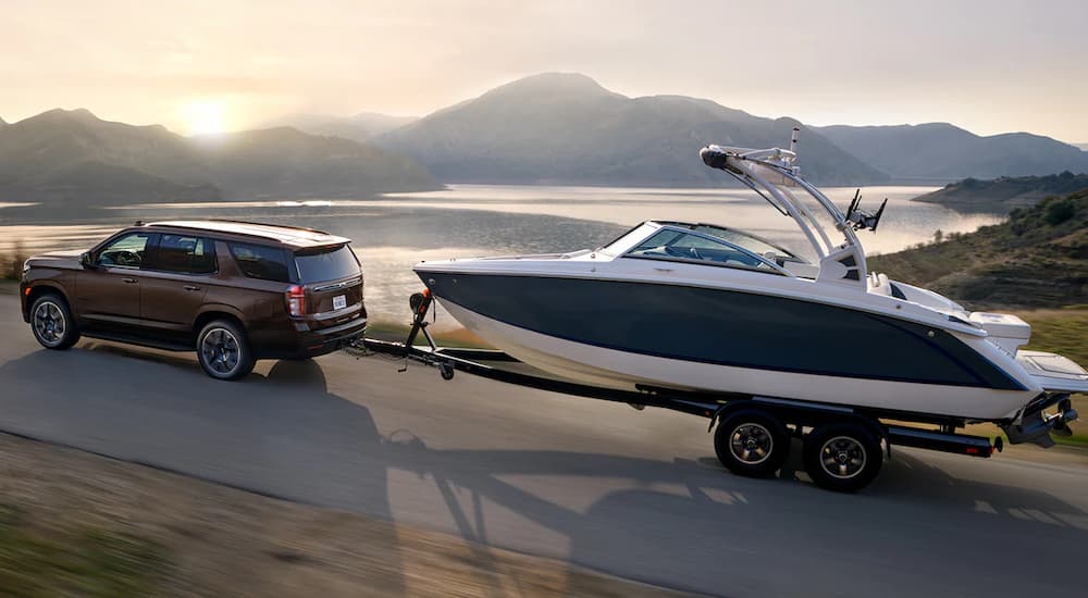 A brown 2022 Chevy Tahoe is shown towing a boat past a lake.