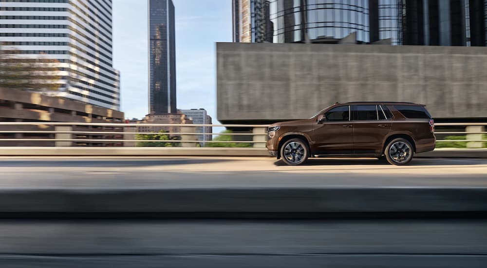 A brown 2022 Chevy Tahoe is shown from the side driving through a city.
