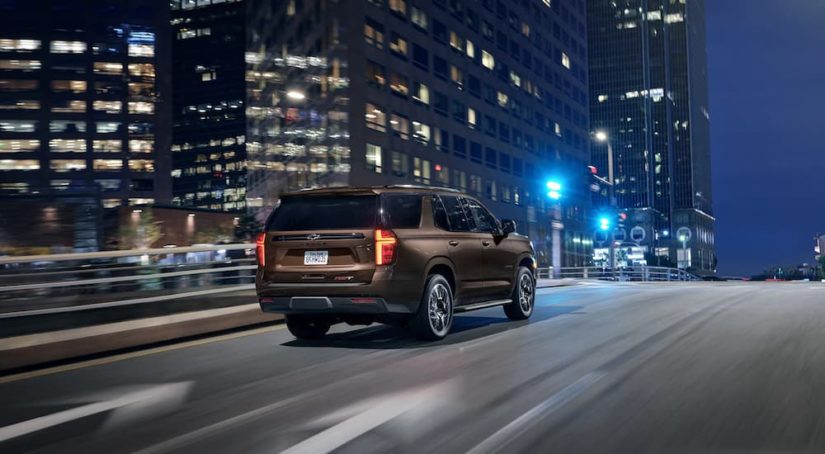 A brown 2022 Chevy Tahoe RST is shown driving on a city street at night.