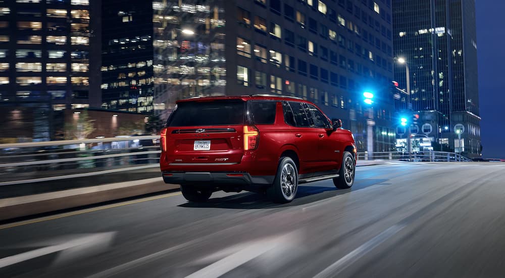 A red 2022 Chevy Tahoe RST is shown from a rear angle driving through a city at night.