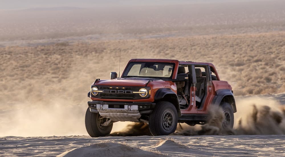 An orange 2022 Ford Bronco Raptor is shown sliding in the desert from the front at an angle.
