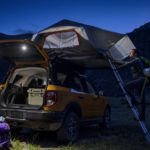 A yellow 2022 Ford Bronco Sport is shown at night as people set up a roof tent.
