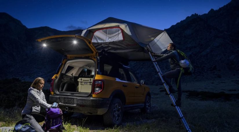 A yellow 2022 Ford Bronco Sport is shown at night as people set up a roof tent.