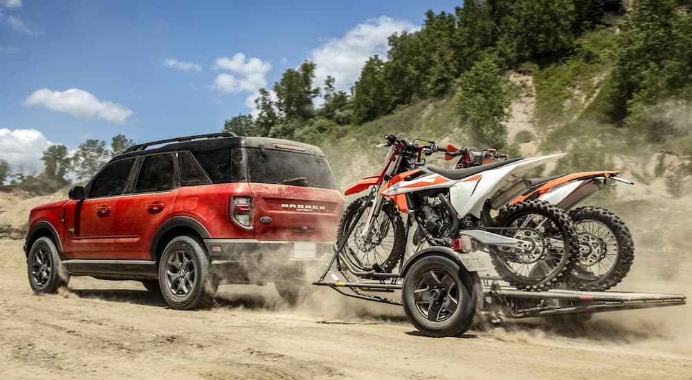 A red 2022 Ford Bronco Sport Outer Banks is shown towing dirt bikes on a dusty trail.