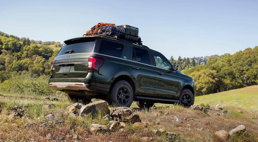 A dark green 2022 Ford Expedition Timberline is shown with luggage on the roof driving on a dirt path.