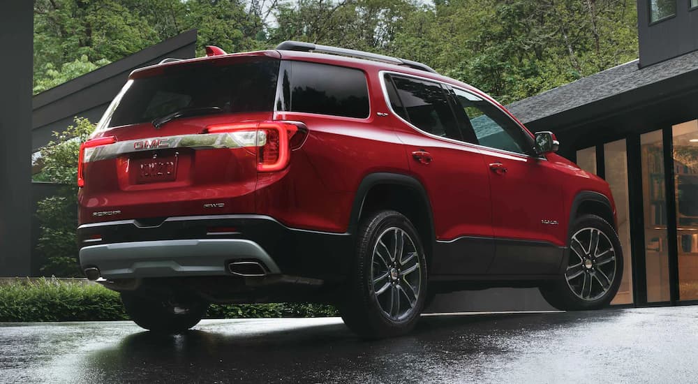 A red 2022 GMC Acadia SLT is shown from a rear angle parked in front of a modern home.