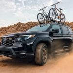 A black 2022 Honda Passport Trailsport is shown driving on a dusty desert path.