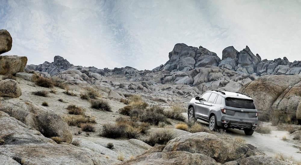 A grey 2022 Honda Passport TrailSport is shown from behind driving up a steep rocky trail.