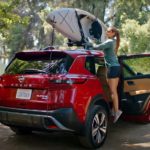 A woman is shown securing a kayak to the roof of a red 2022 Nissan Rogue Platinum.