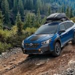 A blue 2022 Subaru Outback Wilderness is shown driving on a rocky mountain path.