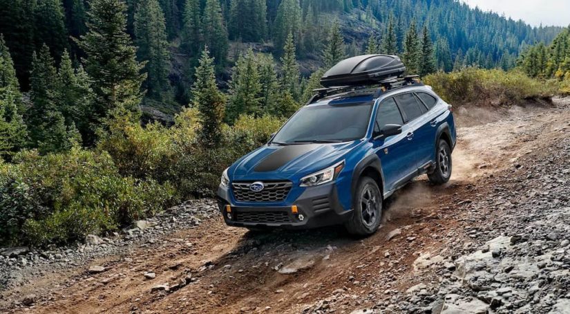 A blue 2022 Subaru Outback Wilderness is shown driving on a rocky mountain path.
