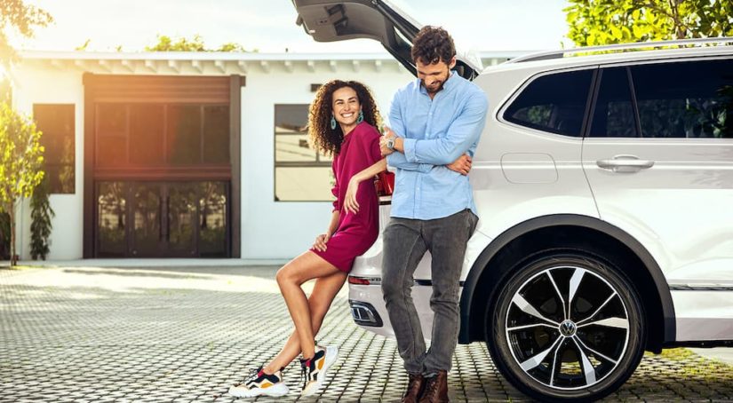 A couple is shown near the rear lift gate of a white 2022 Volkswagen Tiguan.
