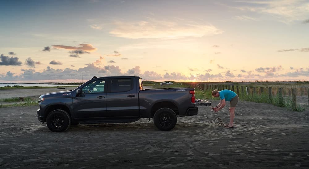 A person is shown with fishing poles leaning on the bed of a 2020 Chevy Silverado 1500 LT Z71 Trail Boss at the beach.