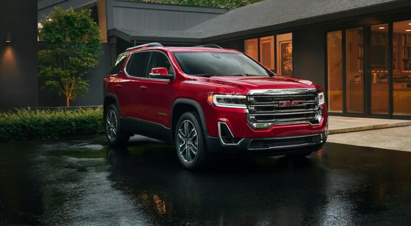 A red 2020 certified pre-owned GMC Acadia is shown parked outside of a modern home.