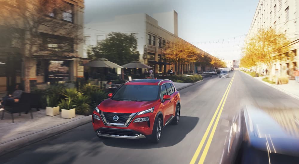 A red 2021 Nissan Rogue is shown driving on a city street after leaving a certified pre-owned Nissan dealer.