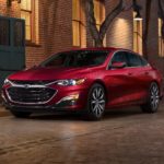 A red 2022 Chevy Malibu is shown parked on a city street after leaving a Chevy dealer.