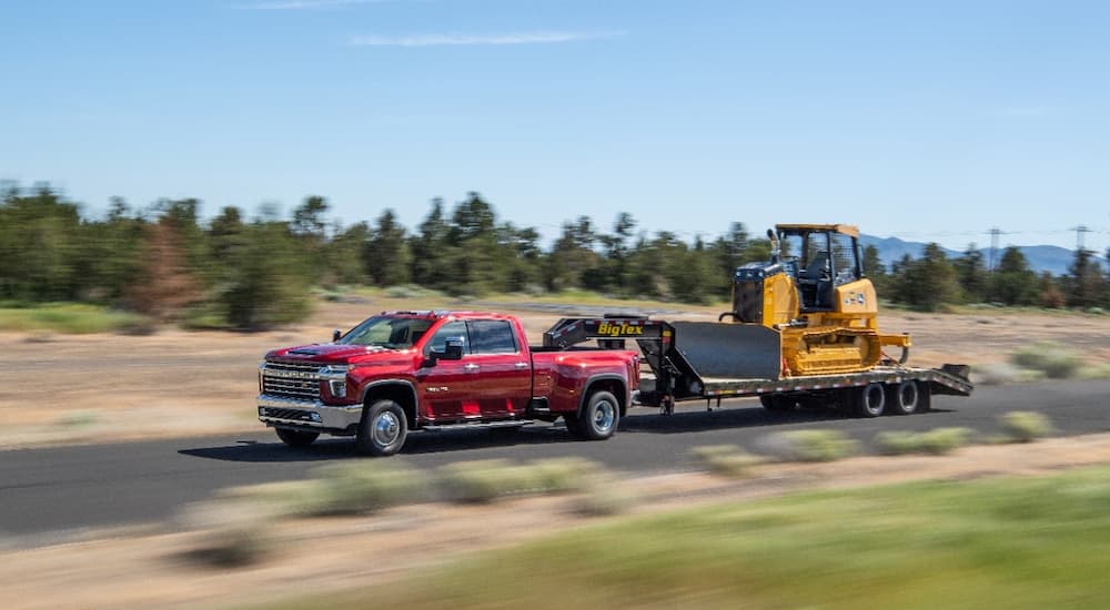A red 2022 Chevy Silverado 3500HD is shown towing heavy machinery. 