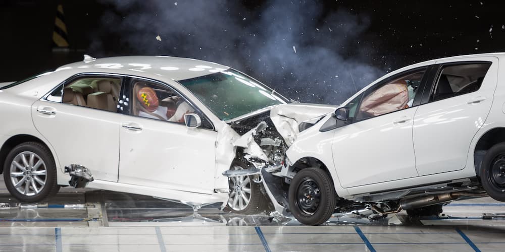 Two white vehicles are shown from the side in a head on collision.