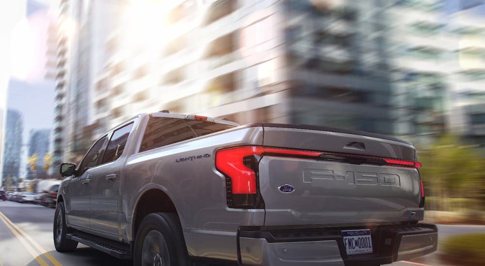 A silver 2022 Ford F-150 Lightning Lariat is shown from a rear angle speeding through a city.