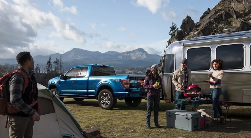 A blue 2022 Ford F-150 STX is shown parked at a campsite towing a silver camper.