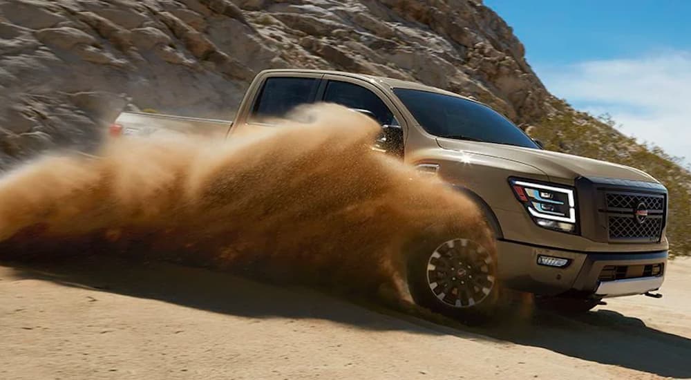 A tan 2020 Nissan Titan is shown kicking up sand in the desert.