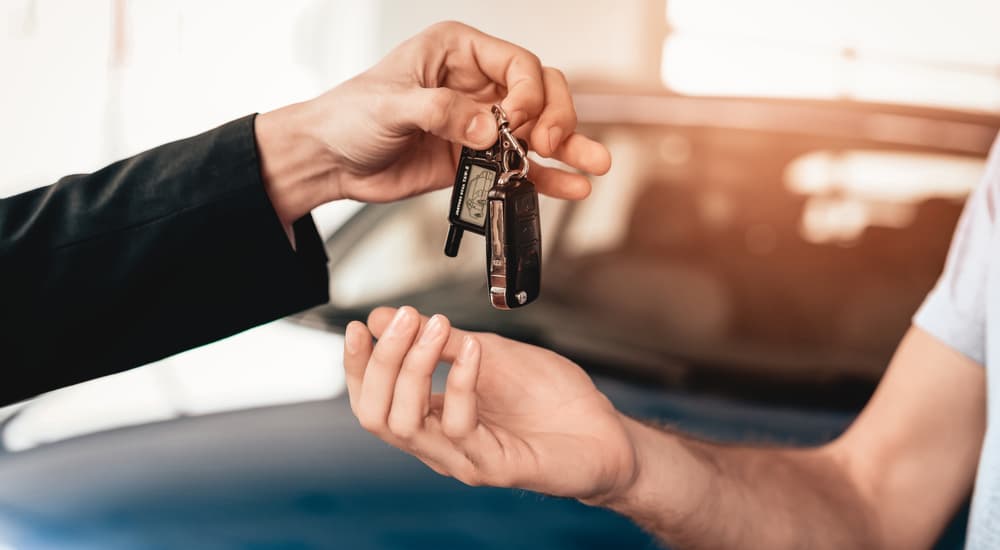 A car salesman is shown handing a set of keys to a customer.
