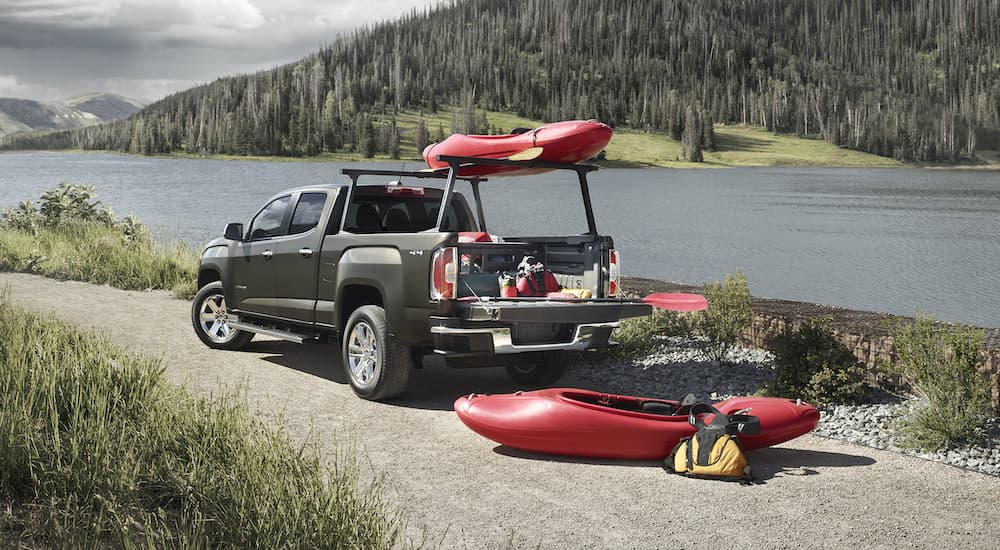 One of the most popular used GMC trucks, a green 2015 GMC Canyon SLT, is shown next to a river unloading kayaks.
