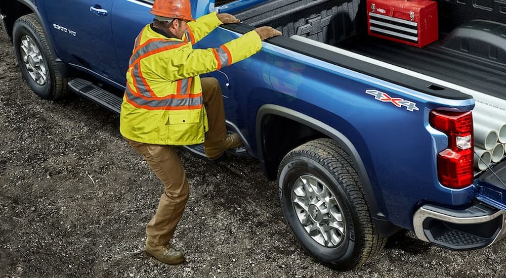 A construction worker is shown stepping into the bed of a blue 2021 Chevy Silverado 1500 WT after leaving a used work truck dealer.